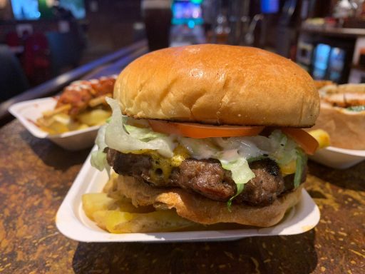 Juicy burger with lettuce, tomato, cheese, and a sesame seed bun, served with fries.