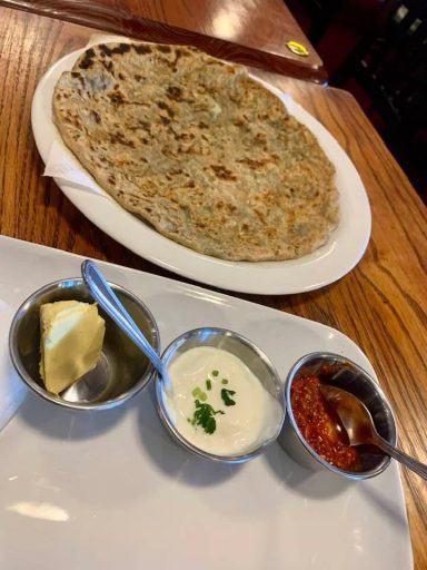 A plate of stuffed flatbread with butter, yogurt, and spicy sauce in small bowls.